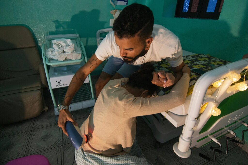 A man supports a woman in labor at a hospital bedside, holding her hand and using a device for comfort.